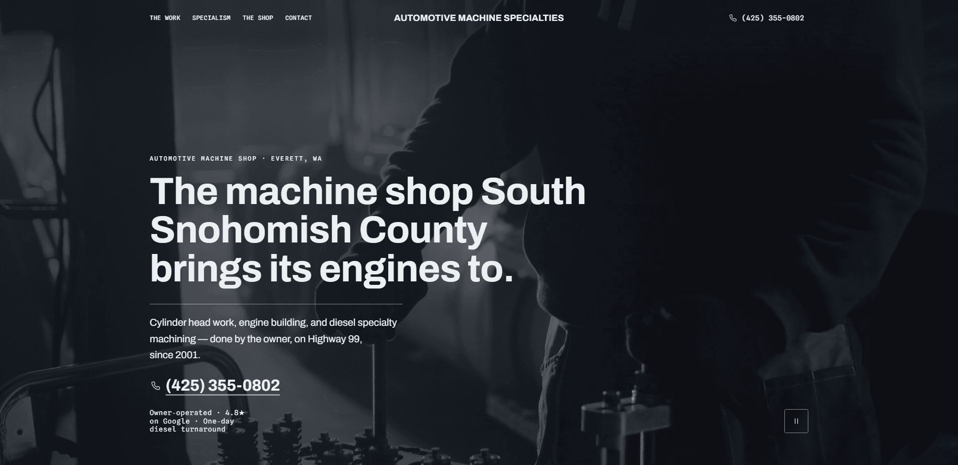 Homepage of Automotive Machine Specialties: a dark, cool-toned video still of a silhouetted machinist at a workbench with valve springs and tooling in the foreground, under a top bar carrying monospace navigation reading The Work, Specialism, The Shop, and Contact, the centered 'Automotive Machine Specialties' wordmark in bold capitals, and a phone number, above the monospace kicker 'Automotive machine shop - Everett, WA', the heavy headline 'The machine shop South Snohomish County brings its engines to.', a thin rule, a paragraph about cylinder head work, engine building, and diesel specialty machining done by the owner on Highway 99 since 2001, a large underlined phone number, a small monospace line noting the shop is owner-operated with one-day diesel turnaround, and a pause control for the background video in the corner.
