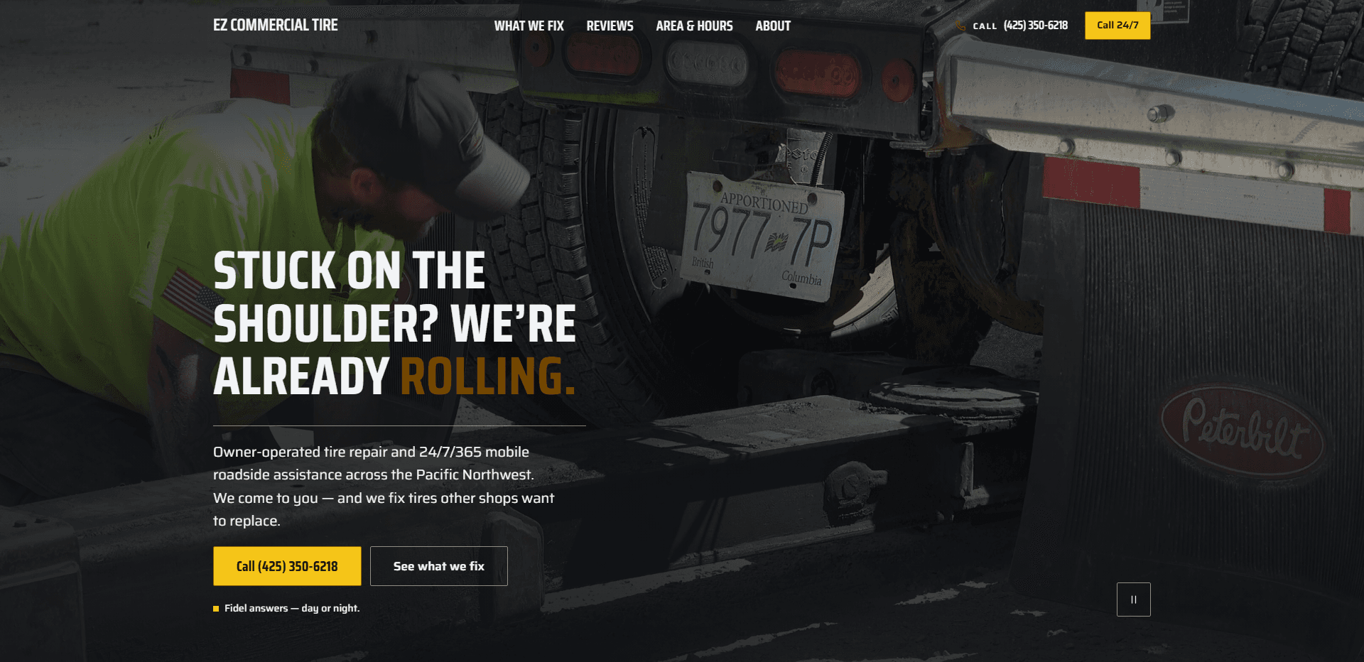 Homepage of EZ Commercial Tire: a dark wash over a video still of a mechanic in a high-visibility green shirt and cap crouched beside the rear dual wheels of a Peterbilt truck, its apportioned British Columbia plate and mud flap in view, under a top bar carrying the condensed 'EZ Commercial Tire' wordmark, navigation reading What we fix, Reviews, Area & hours, and About, a 'Call' phone number, and a yellow 'Call 24/7' button, above the oversized condensed capitals headline 'Stuck on the shoulder? We're already rolling.' with its last word in amber, a line about owner-operated tire repair and 24/7/365 mobile roadside assistance across the Pacific Northwest, a yellow 'Call' button with the phone number beside an outlined 'See what we fix' button, the small line 'Fidel answers - day or night.', and a pause control for the background video in the corner.