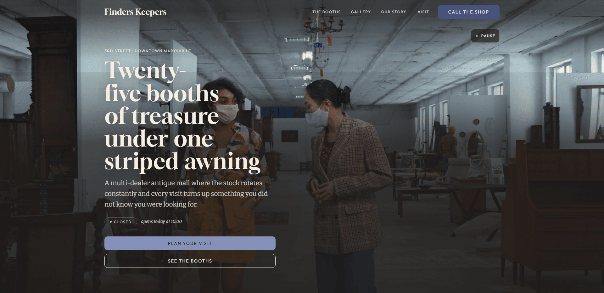 Homepage of Finders Keepers: a dark wash over a video still of two women in face masks talking in the aisle of a long, white-walled antique warehouse lined with dark wood furniture beneath a hanging chandelier, under a top bar carrying the serif 'Finders Keepers' wordmark, navigation reading The booths, Gallery, Our story, and Visit, and a periwinkle 'Call the shop' button, above the kicker '3rd Street - Downtown Marysville', the large serif headline 'Twenty-five booths of treasure under one striped awning', a line about a multi-dealer antique mall where the stock rotates constantly, a 'Closed' status pill beside the italic line 'opens today at 10:00', a full-width periwinkle 'Plan your visit' button stacked above an outlined 'See the booths' button, and a pause control for the background video in the corner.