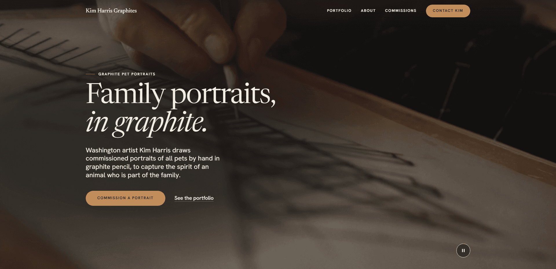 Homepage of Kim Harris Graphites: a dim, warm video still of a hand drawing with a graphite pencil on paper across a wooden drawing board, under a top bar carrying the serif 'Kim Harris Graphites' wordmark, navigation reading Portfolio, About, and Commissions, and a tan 'Contact Kim' button, above the kicker 'Graphite pet portraits', the large serif headline 'Family portraits, in graphite.' with its second line in italic, a paragraph about Washington artist Kim Harris drawing commissioned portraits of all pets by hand in graphite pencil, a tan 'Commission a portrait' button beside a 'See the portfolio' link, and a pause control for the background video in the corner.