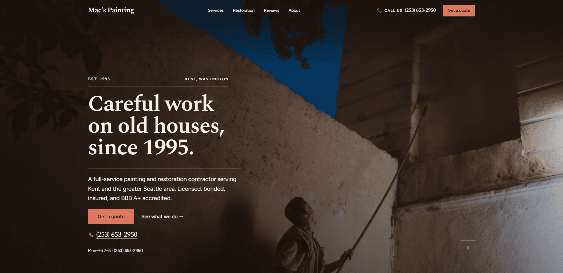Homepage of Mac's Painting: a dark wash over a video still of a painter looking up as he reaches a long red roller pole toward the eaves of a weathered cream stucco wall, under a slice of deep blue sky and overhanging leaves, beneath a top bar carrying the serif 'Mac's Painting' wordmark, navigation reading Services, Restoration, Reviews, and About, a 'Call us' phone number, and a coral 'Get a quote' button, above the paired kicker 'Est. 1995' and 'Kent, Washington' over a fine rule, the large serif headline 'Careful work on old houses, since 1995.', a paragraph about a full-service painting and restoration contractor serving Kent and the greater Seattle area, a coral 'Get a quote' button beside a 'See what we do' arrow link, the phone number in serif type, an hours line reading 'Mon-Fri 7-5', and a pause control for the background video in the corner.