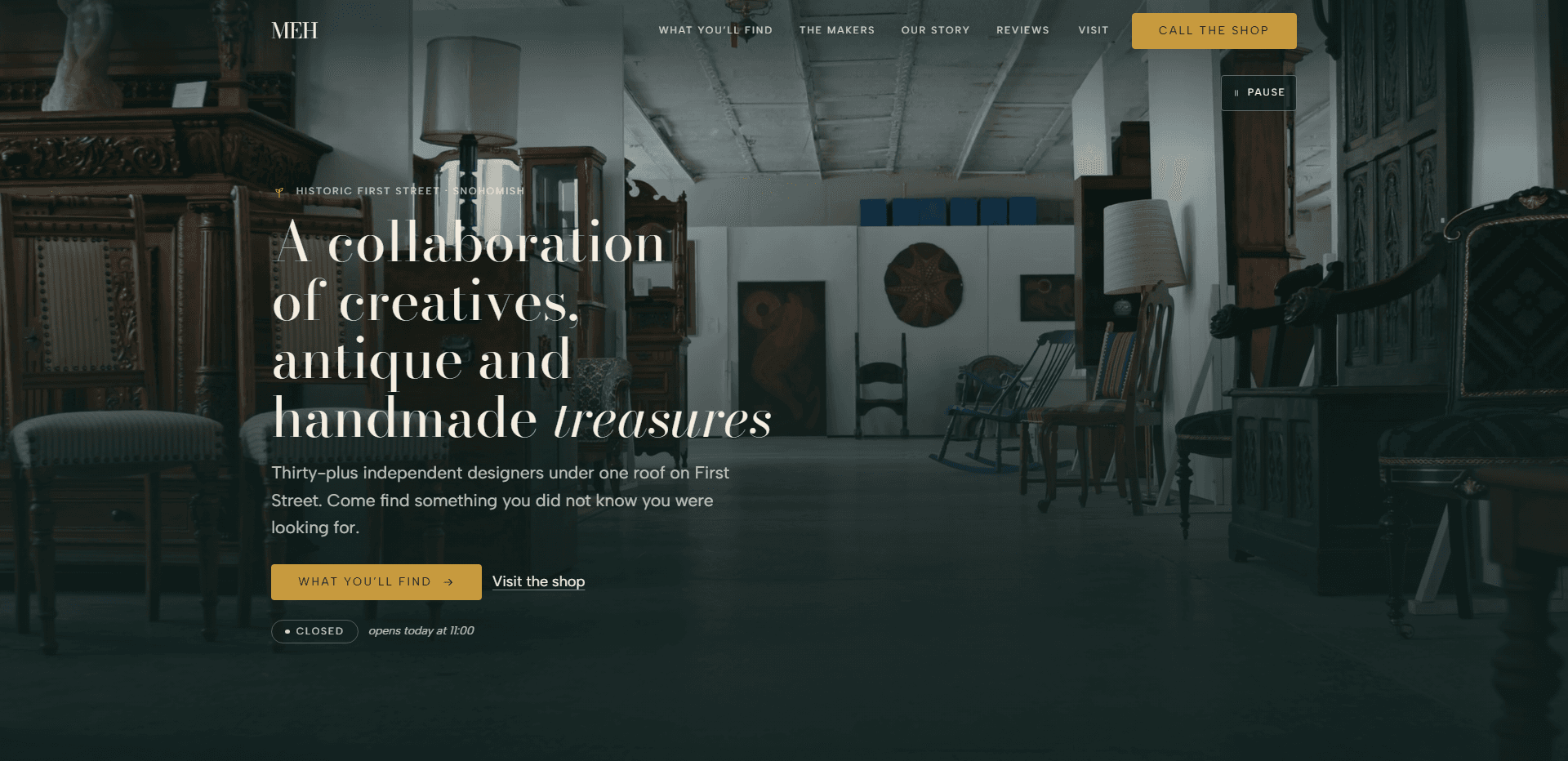Homepage of My Eclectic Home: a dark teal wash over a video still of an antique showroom filled with carved dark wood cabinets, tall lamps, wooden and rocking chairs, and framed art on white walls, under a top bar carrying the serif 'MEH' monogram, navigation reading What you'll find, The makers, Our story, Reviews, and Visit, and a gold 'Call the shop' button, above a small sprig mark and the kicker 'Historic First Street - Snohomish', the large high-contrast serif headline 'A collaboration of creatives, antique and handmade treasures' with its last word in italic, a line about thirty-plus independent designers under one roof on First Street, a gold 'What you'll find' button with an arrow beside a 'Visit the shop' link, a 'Closed' status pill beside the italic line 'opens today at 11:00', and a pause control for the background video in the corner.