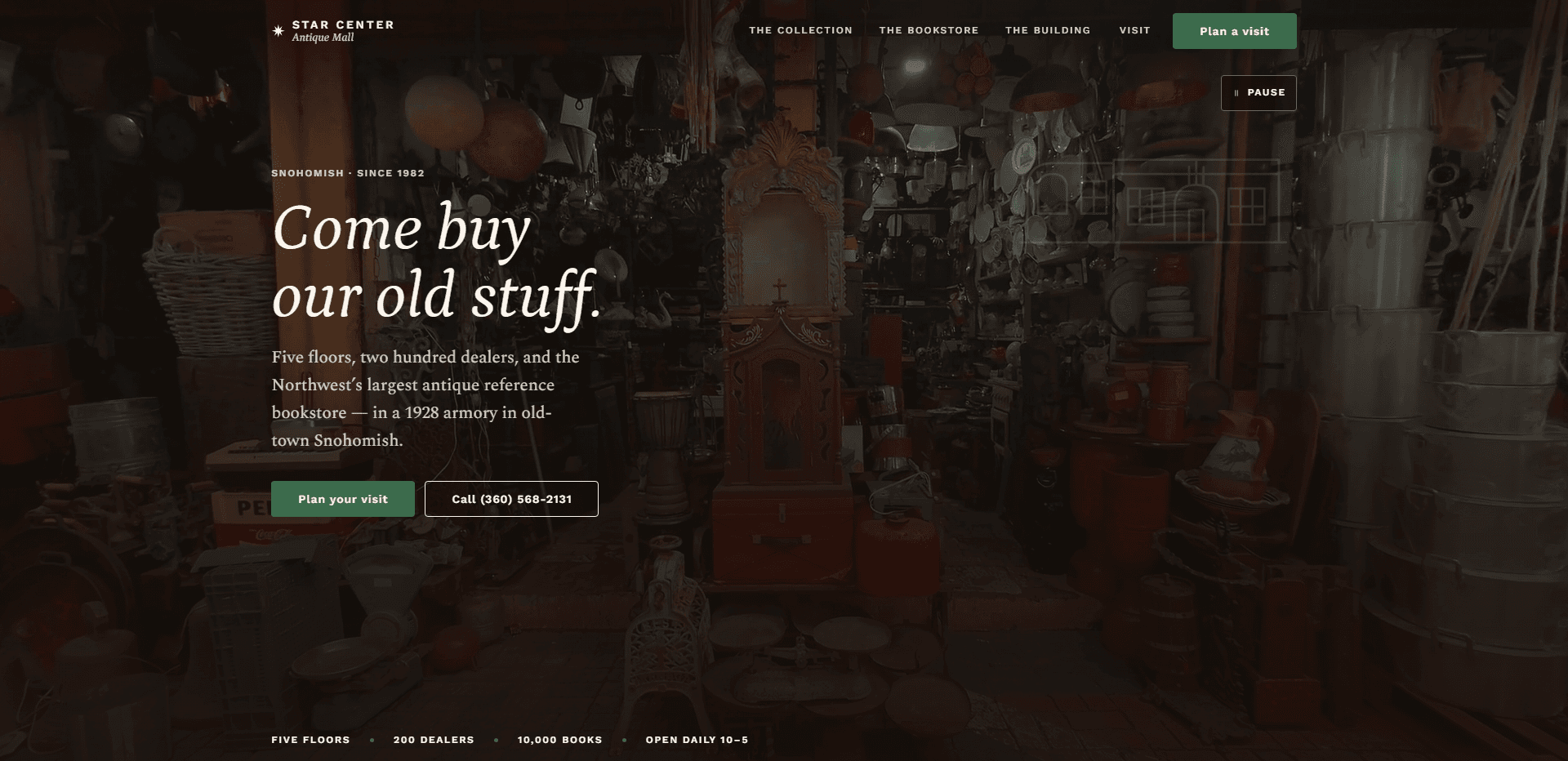 Homepage of Star Center Antique Mall: a dim video still of a crowded aisle of antiques - hanging lamps, enamel plates, galvanized tubs, and an ornate carved wooden cabinet - with a faint line drawing of a building facade in the upper corner, under a top bar carrying a star mark beside the 'Star Center Antique Mall' wordmark, navigation reading The Collection, The Bookstore, The Building, and Visit, a green 'Plan a visit' button, and a pause control for the background video beneath it, above the kicker 'Snohomish - Since 1982', the large italic serif headline 'Come buy our old stuff.', a paragraph about five floors, two hundred dealers, and an antique reference bookstore in a 1928 armory in old-town Snohomish, a green 'Plan your visit' button beside an outlined 'Call' phone number button, and a row along the bottom reading Five floors, 200 dealers, 10,000 books, and Open daily 10-5.