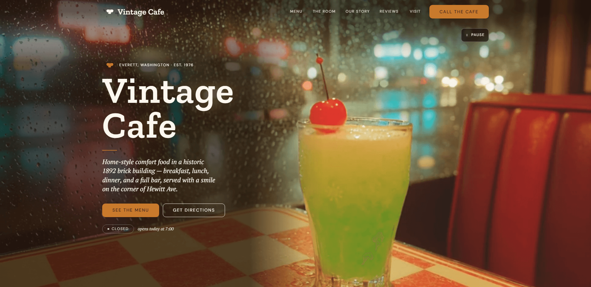 Homepage of Vintage Cafe: a video still of a bright green soda topped with a maraschino cherry on a red-and-cream checkered table beside a red vinyl booth, with blurred neon city lights through a rain-speckled window behind, under a top bar carrying a small amber emblem beside the serif 'Vintage Cafe' wordmark, navigation reading Menu, The room, Our story, Reviews, and Visit, and an amber 'Call the cafe' button, above the kicker 'Everett, Washington - Est. 1976', the oversized serif headline 'Vintage Cafe' over a short amber rule, an italic line about home-style comfort food in a historic 1892 brick building, with breakfast, lunch, dinner, and a full bar on the corner of Hewitt Ave, an amber 'See the menu' button beside an outlined 'Get directions' button, a 'Closed' status pill beside the italic line 'opens today at 7:00', and a pause control for the background video in the corner.